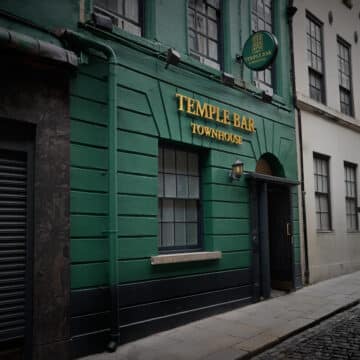 A green building with "Temple Bar Townhouse" sign in gold letters above the door on a cobblestone street.