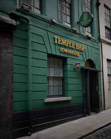A green building with "Temple Bar Townhouse" sign in gold letters above the door on a cobblestone street.