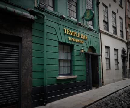 A green building with "Temple Bar Townhouse" sign in gold letters above the door on a cobblestone street.