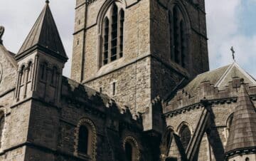 A stone Gothic-style church with pointed arches, tall windows, and a central bell tower against a partly cloudy sky.