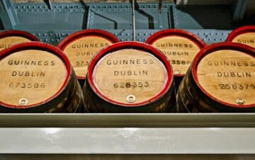 Wooden barrels labeled "Guinness Dublin" with serial numbers are stacked on their sides in a storage area.