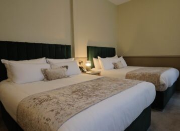 Spacious hotel room with two plush double beds, elegant decor, soft lighting, and luxury bedding for a comfortable stay.
