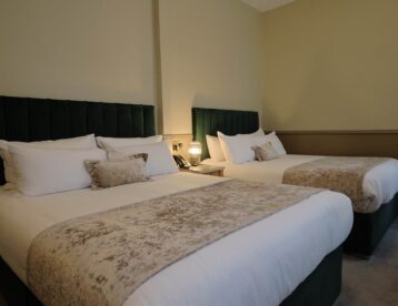 Spacious hotel room with two plush double beds, elegant decor, soft lighting, and luxury bedding for a comfortable stay.