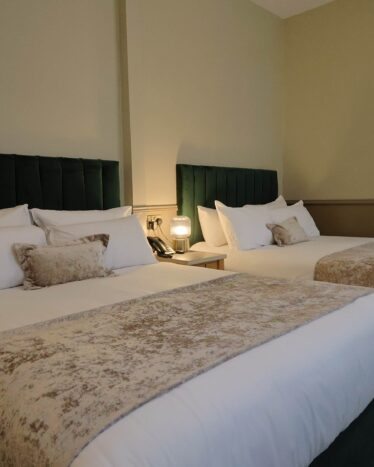 Spacious hotel room with two plush double beds, elegant decor, soft lighting, and luxury bedding for a comfortable stay.