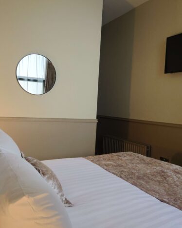 Cosy hotel room with plush bed, round mirror, wall-mounted TV, and clothes rack, perfect for a relaxing stay.