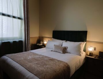 Cosy hotel room with plush double bed, soft lighting, elegant decor, and bedside table; perfect for a relaxing stay.