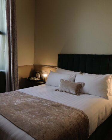 Cosy hotel room with plush double bed, soft lighting, elegant decor, and bedside table; perfect for a relaxing stay.